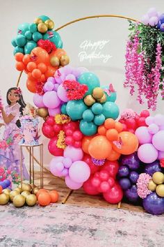 a birthday party with balloons and flowers on the table, in front of an arch