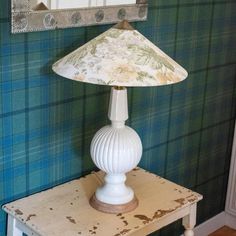 a white lamp sitting on top of a wooden table next to a green plaid wall