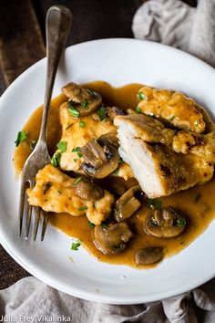 a white plate topped with chicken covered in mushroom gravy next to a fork