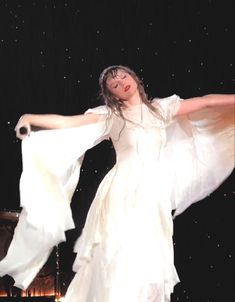 a woman in white dress standing on stage with her arms spread out to the side