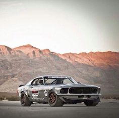 an old mustang sits parked in front of mountains