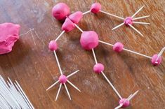 pink marshmallows and toothpicks are arranged on a wooden table with yarn