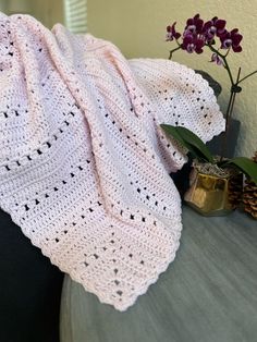 a white crocheted blanket sitting on top of a table next to a potted plant