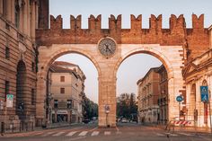 an arch with a clock on it in the middle of a street between two buildings