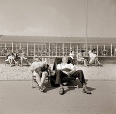 two people sitting on chairs in front of a building with lots of windows and one person holding a dog