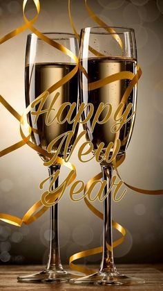 two glasses of champagne with gold ribbon and happy new year lettering on the glass are ready to be toasted