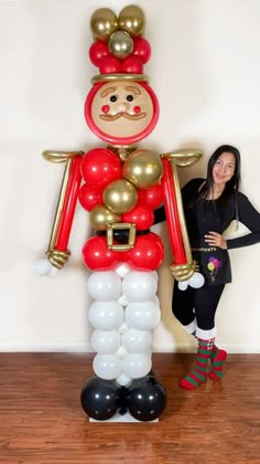 a woman standing next to a giant balloon dressed up like a nutcracker with gold, red and white balloons