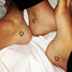 two people laying in bed with their feet crossed and hearts tattooed on the sides of their legs