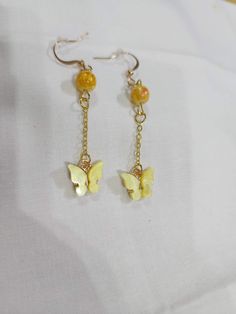 Yellow butterfly hanging from a gold colored chain with a yellow accent bead Gold Plated Beaded Dangle Jewelry, Gold Plated Dangle Jewelry With Beaded Chain, 14k Gold Filled Chain Dangle Earrings, Yellow Jewelry With Butterfly Charm For Gift, Gold Metal Earrings With Butterfly Charm, Metal Earrings With Gold Chain For Gift, Gold Earrings With Butterfly Charm, Yellow Gold Butterfly Jewelry With Piercing, Trendy Gold Jewelry With Dangling Beads