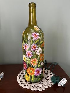 a green vase with flowers painted on it sitting on a doily next to a charger