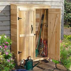 a garden shed with its doors open and gardening tools in the ground next to it