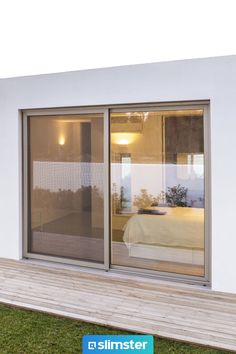 an open sliding glass door on the side of a house with grass in front of it