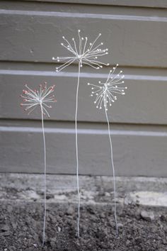 two metal dandelions sitting on top of dirt next to a building and grass