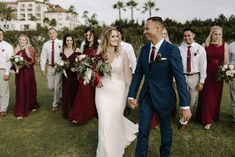 a bride and groom walk through the grass with their wedding party