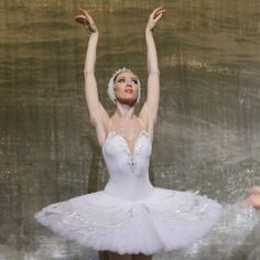 ballerina in white tutu with arms raised above head and hands behind her back