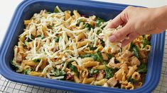 a person is sprinkling parmesan cheese on top of pasta in a blue casserole dish