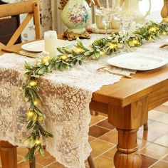 the table is set for christmas dinner with candles and greenery garlands on it