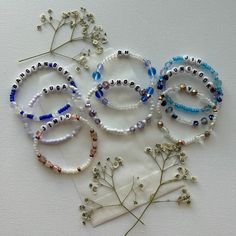 several bracelets with beads and flowers on a white tablecloth next to each other