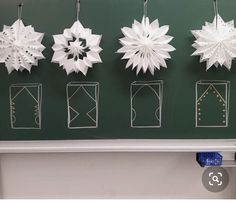 paper snowflakes are hanging on the wall in front of a chalkboard with writing