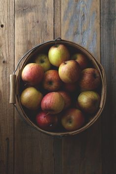 a basket full of apples sitting on top of a wooden table next to a wall