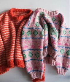 two knitted sweaters sitting next to each other on top of a white surface