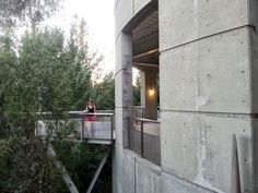 a woman standing on a bridge over a river next to a building with trees in the background