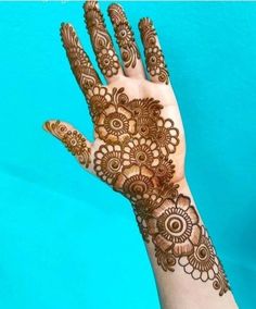 a hand with henna on it and some flowers in the middle, against a blue background