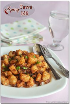 a white plate topped with tater tots next to a fork and glass of water