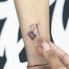 a small tattoo on the wrist of a woman's left arm, with a sewing needle and spool