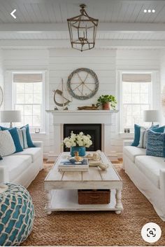 a living room with white couches and blue pillows on top of the sofas