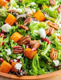 a salad in a wooden bowl with pecans and feta cheese on the side