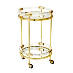 a round glass and brass bar cart with wheels on the bottom is shown in front of a white background