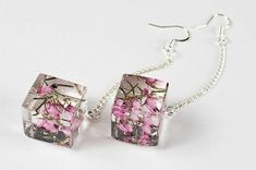 two pink flowers are attached to silver earrings on a white surface, with one dangling from a chain