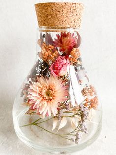 a vase filled with flowers on top of a white table next to a cork covered bottle