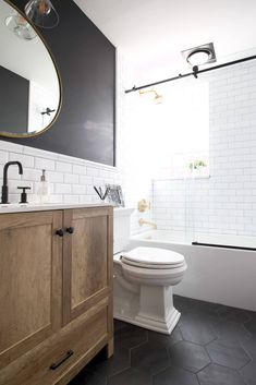 a white toilet sitting next to a wooden cabinet in a bathroom under a round mirror