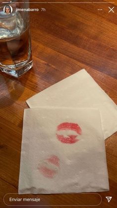 two pieces of paper with red lipstick on them next to a glass of water and napkins