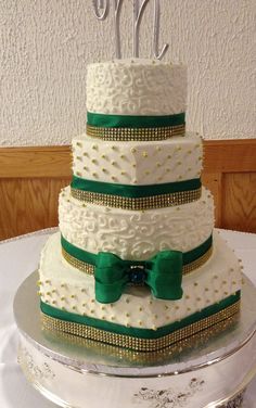 a three tiered wedding cake with green ribbon and bow on the top is sitting on a silver platter