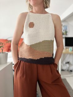 a woman wearing brown pants and a crocheted tank top standing in front of a desk