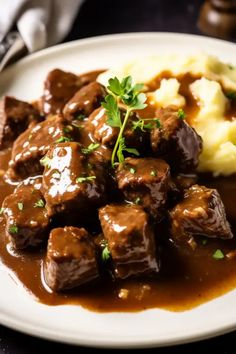 a white plate topped with meat and gravy next to mashed potatoes