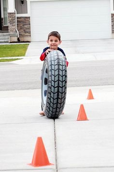 a young boy is playing with a large tire on the sidewalk in front of some orange cones