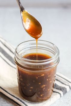 a spoon full of bbq sauce being drizzled over the top of a jar