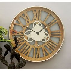 a wooden clock with roman numerals on the face next to a potted plant