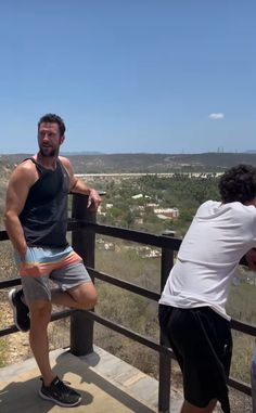 a man standing on top of a metal rail next to another man in shorts and tank top