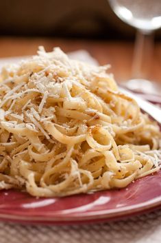 a red plate topped with pasta and parmesan on top of a wooden table