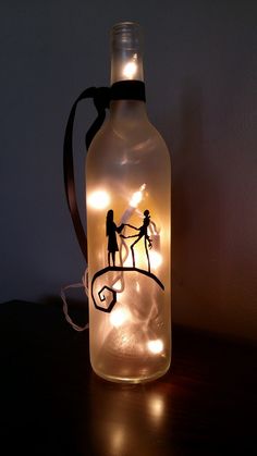 a lighted bottle with two people holding hands and string lights attached to the top, on a table