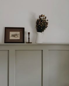 a white vase with flowers on top of a mantle