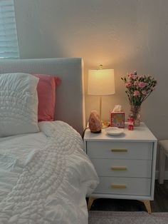 a white bed sitting next to a night stand with flowers on it and a lamp