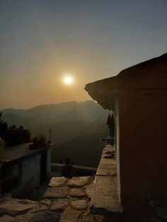 the sun is setting on top of a hill with mountains in the background and people walking up to it