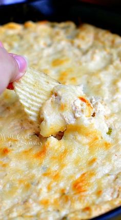 a hand dipping a tortilla chip into a skillet filled with quesadilla