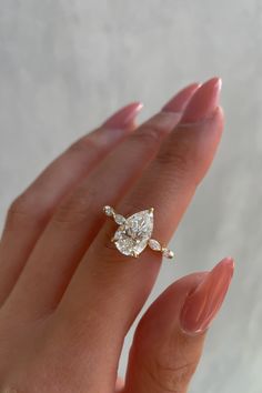 a woman's hand holding an engagement ring with a pear shaped diamond on it